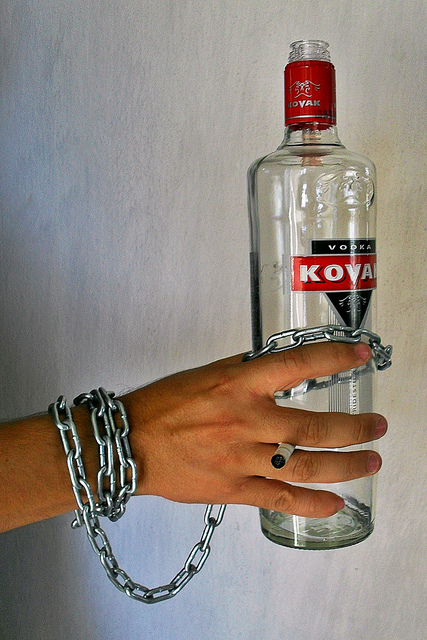 Man's wrist chained to a bottle of alcohol